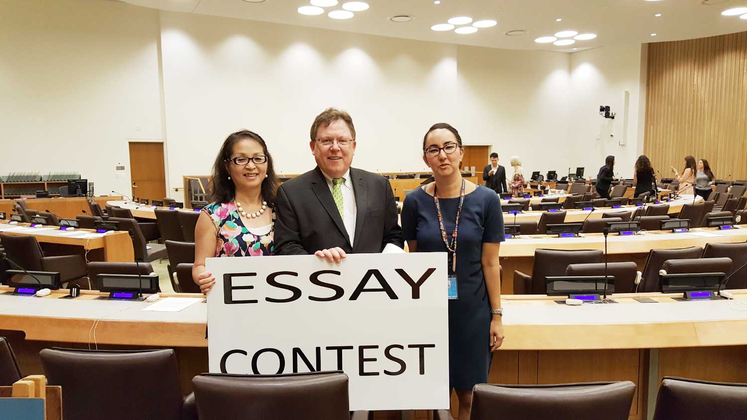 Photo: 3 adults in conference room with Essay Contest sign