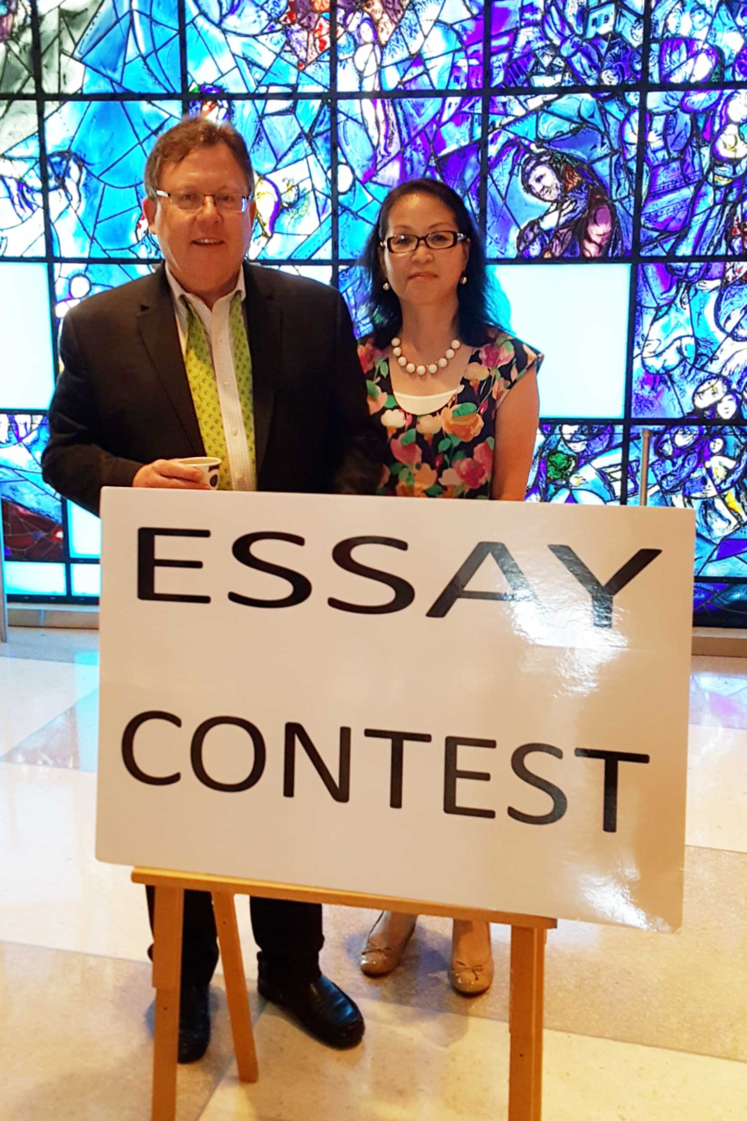 Photo: Mitsuki and Stephen Post with Essay Contest sign and stained glass